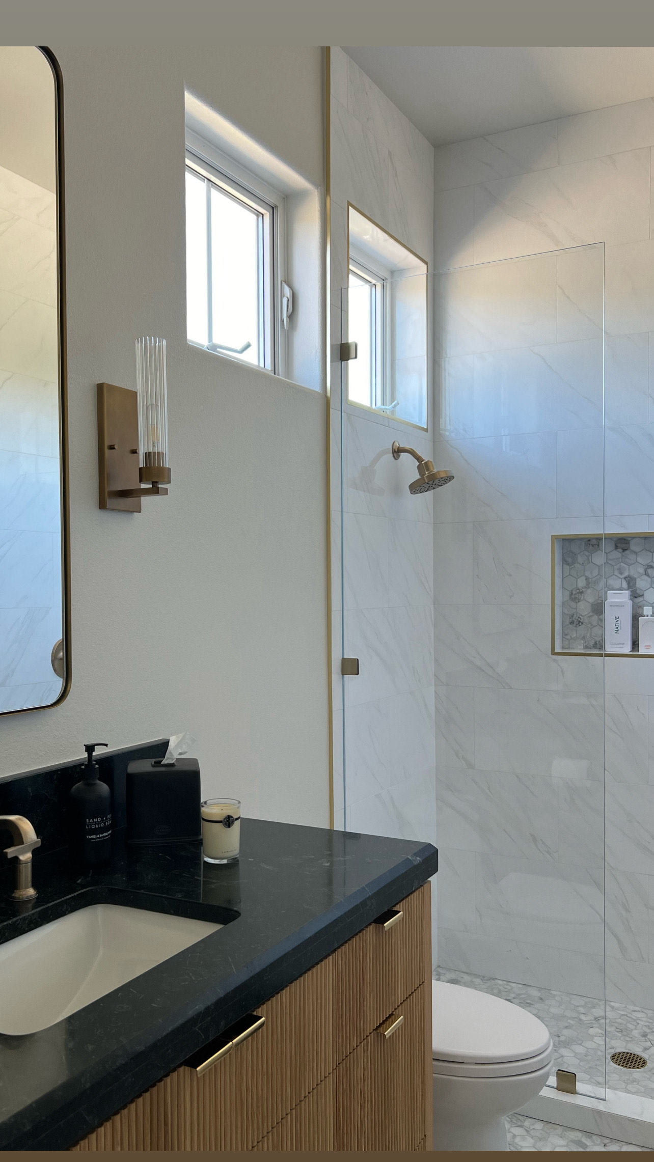 Vanity and shower with brass accents and stone tile