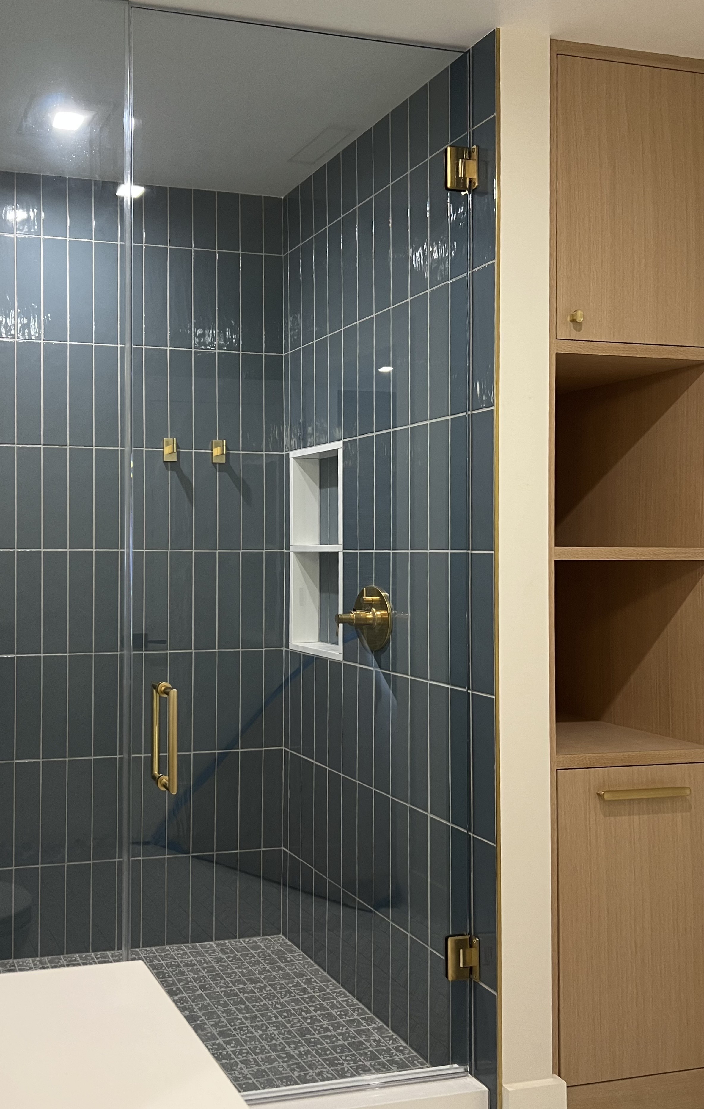 Shower with tall vertical blue tile and brass fixtures
