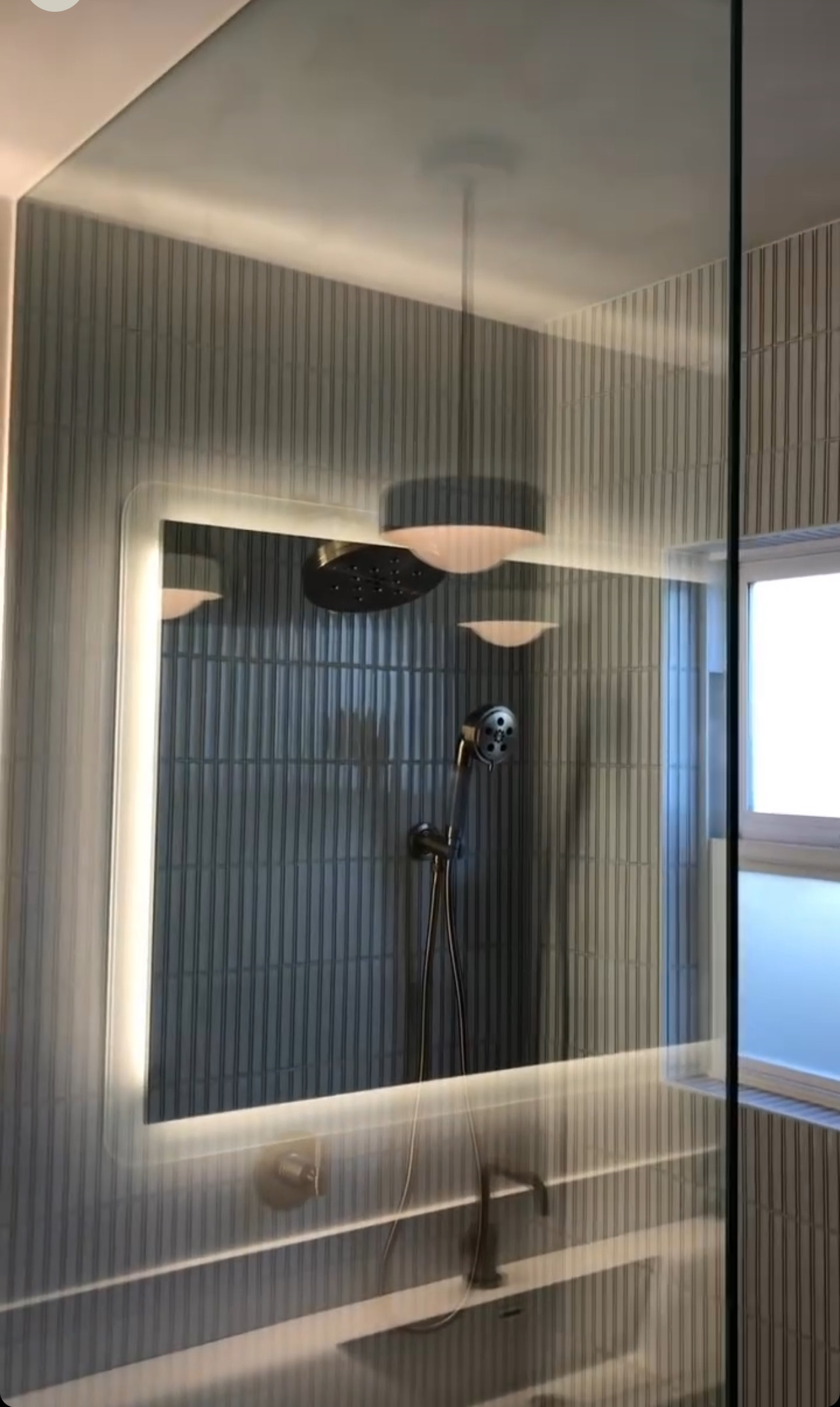 Reflective shower glass showing lighted mirror and fixtures
